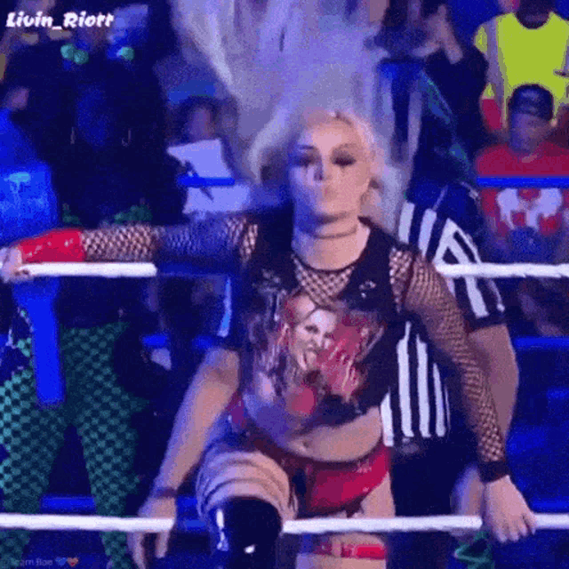 a woman is standing in a wrestling ring with her arms outstretched and a referee behind her .