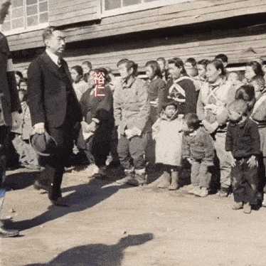 a man in a suit stands in front of a group of people with chinese writing on their shirts