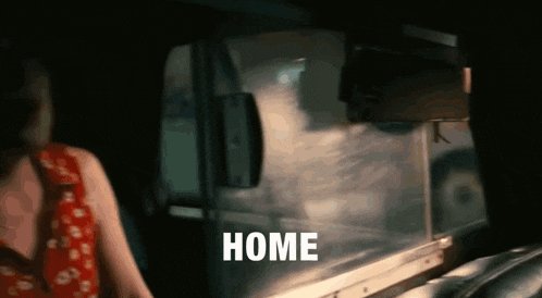 a woman in a red dress is standing in a dark room with the word home written on the window