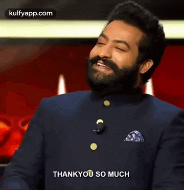 a man with a beard is standing in front of a microphone and saying thank you so much .