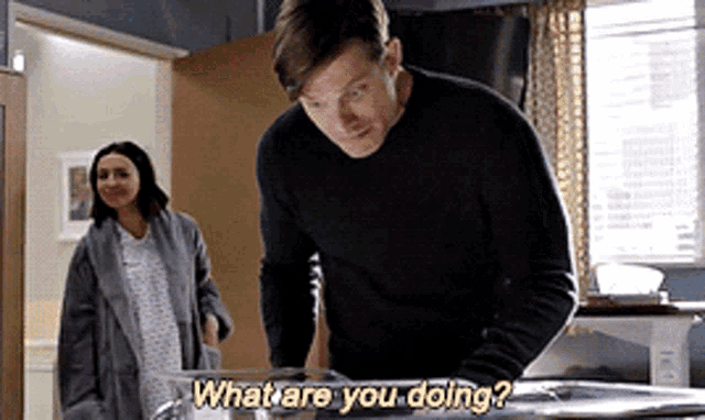 a man in a black sweater is standing in front of a woman in a hospital gown and asking what are you doing