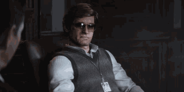 a man wearing sunglasses and a name tag that says 13.9 sits in a chair