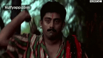 a man with a mustache and a red bindi on his forehead is standing in front of a woman .