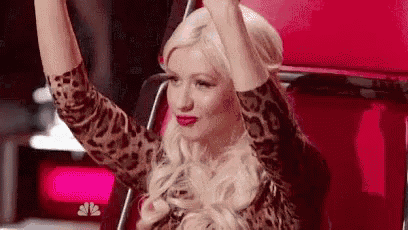 a woman in a leopard print shirt is sitting in a red chair with her hands in the air .