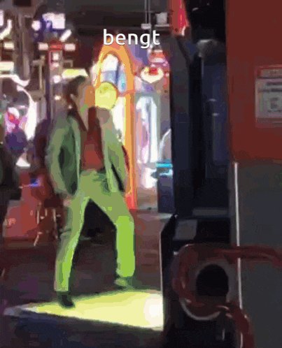 a man in green pants is standing in front of an arcade machine with the word bengt on the bottom right
