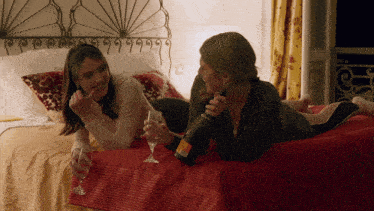 two women laying on a bed with a bottle of veuve clicquot in front of them