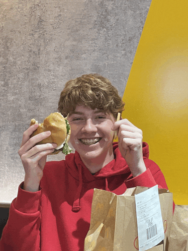a young man in a red hoodie is eating a hamburger