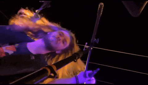 a man with long hair is standing in front of a microphone with a purple background