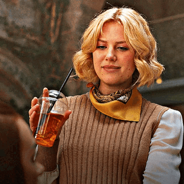 a woman wearing a brown vest and a yellow scarf is holding a glass with a straw