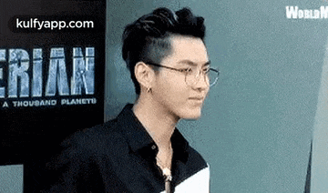 a man wearing glasses and a black shirt is standing in front of a sign that says a thousand planets .