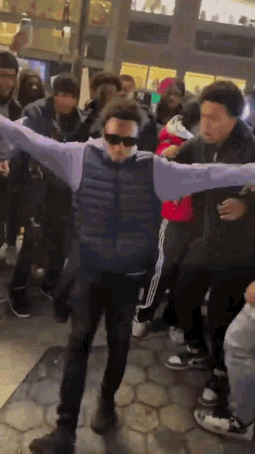 a man wearing sunglasses is dancing in front of a crowd .