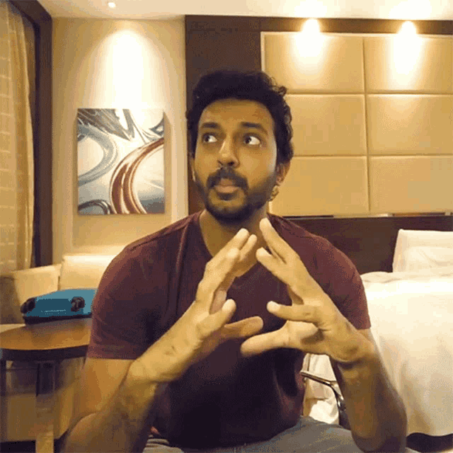 a man with a beard is making a gesture with his hands in front of a bed