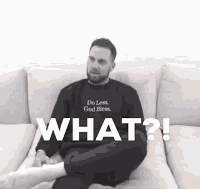 a man is sitting on a couch wearing a sweater that says " do less god bless "