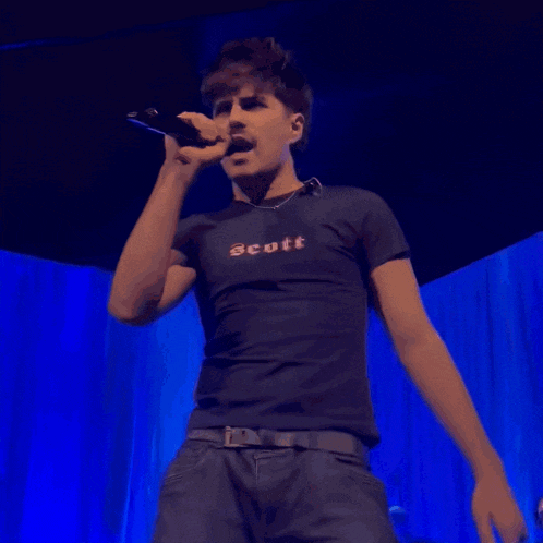 a man is singing into a microphone wearing a scott shirt