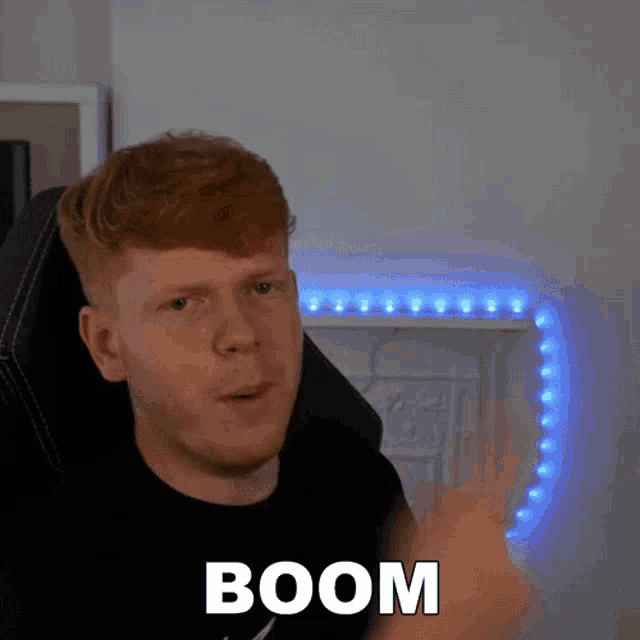 a man with red hair and a black shirt is pointing at something with the word boom on it