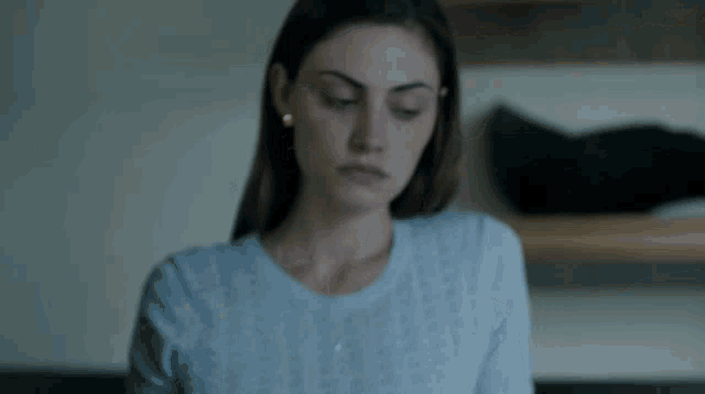 a woman wearing a blue sweater and earrings looks down at something .