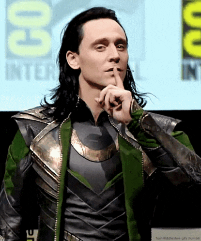 a man in a costume holds his finger to his mouth in front of a sign that says comic con