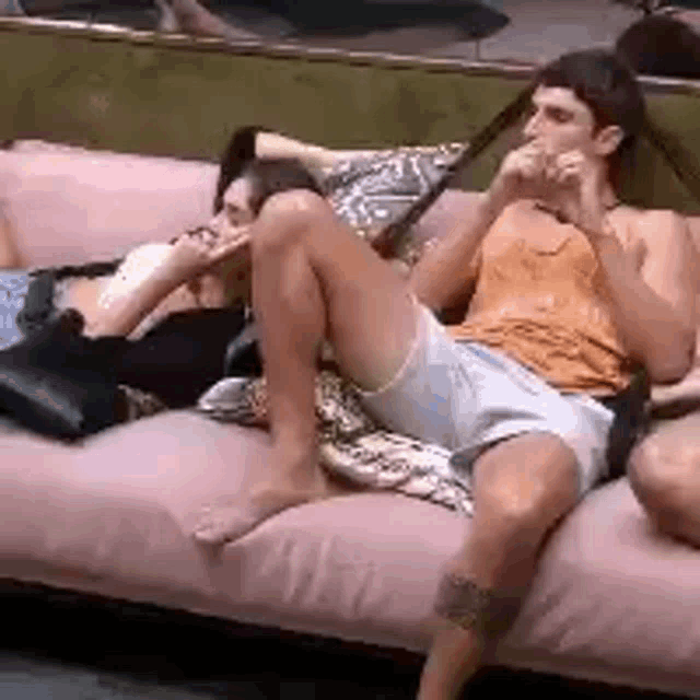 a man is sitting on a pink couch with his legs crossed and a woman is sitting next to him .