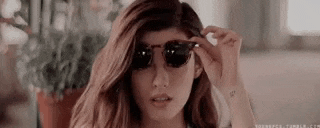a woman wearing sunglasses is standing in front of a window .