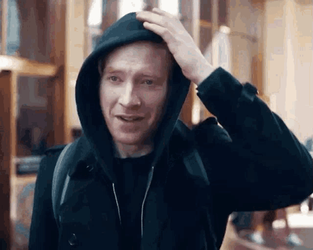 a man wearing a black hooded jacket scratches his head