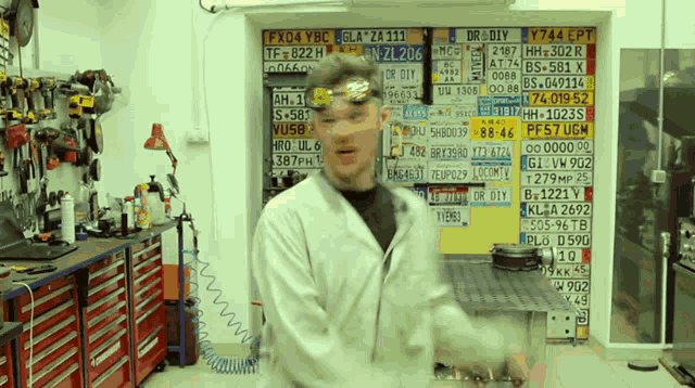 a man in a lab coat is standing in front of a wall of license plates including one that says fx04 ybc
