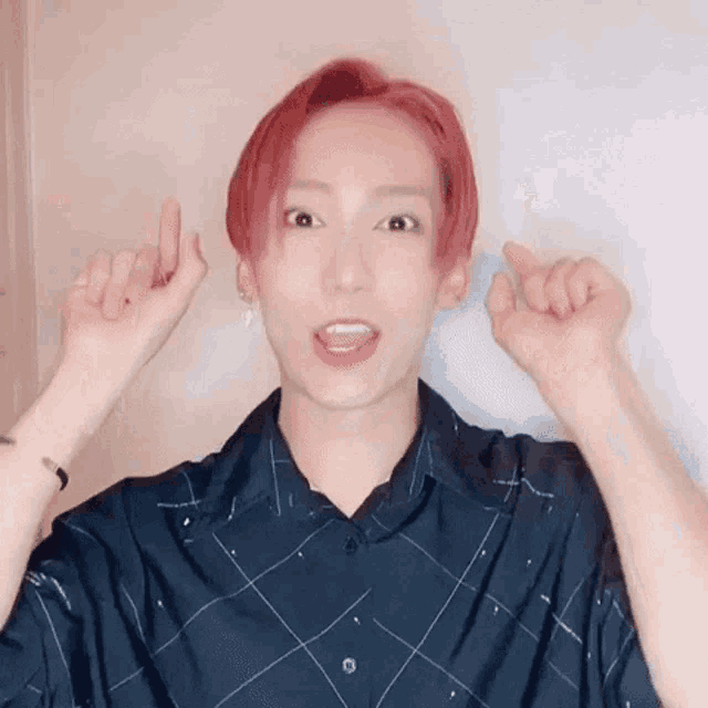 a young man with red hair and a black shirt is making a heart with his hands .