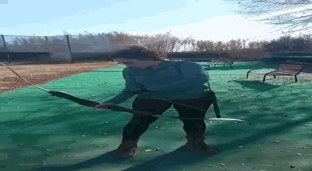 a woman is holding a bow and arrow on a green court .