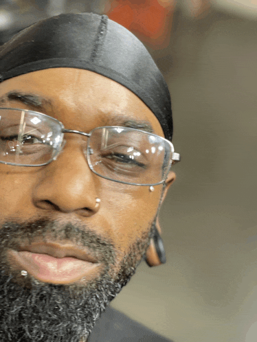 a man with glasses and a beard is wearing a black cap