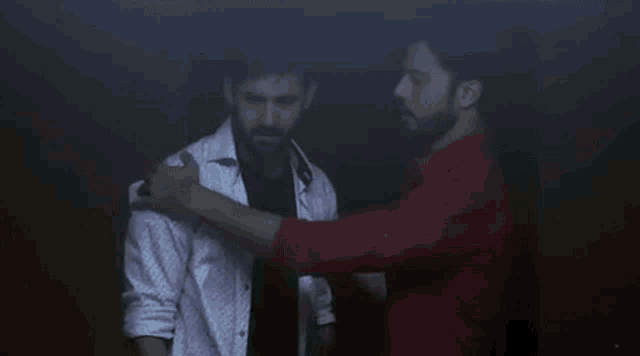 two men are standing next to each other in a dark room looking at each other .