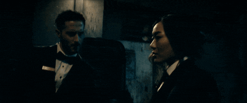a man in a tuxedo and bow tie stands next to a woman in a tuxedo