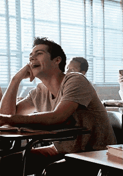a man is sitting at a desk in a classroom with his hands on his chin .