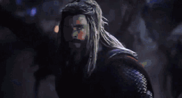 a man with long hair and a beard is holding a hammer and a shield .