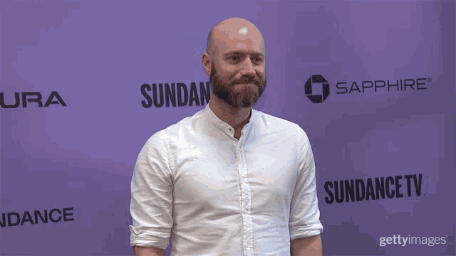 a bald man with a beard is standing in front of a purple background that says sundance