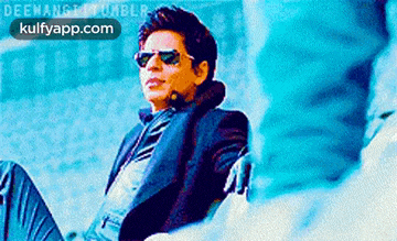 a man in a suit and sunglasses is sitting on a couch with his legs crossed .
