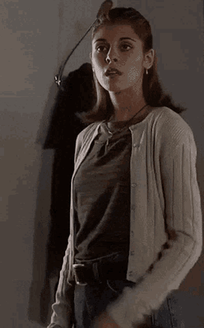 a woman wearing a cardigan and jeans is standing in a dark room .