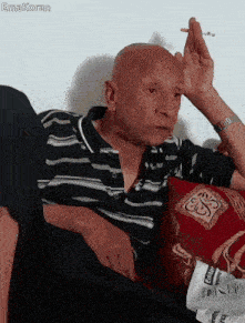 a bald man is smoking a cigarette while sitting on a couch