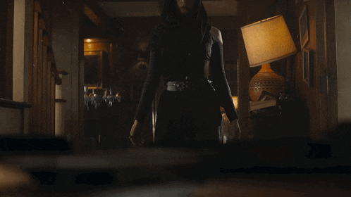 a woman in a black outfit stands in a dark room