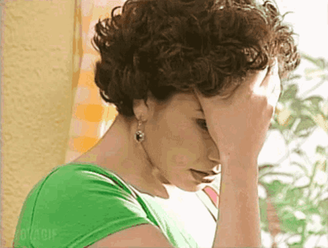 a woman with curly hair is covering her face with her hand while wearing a green shirt