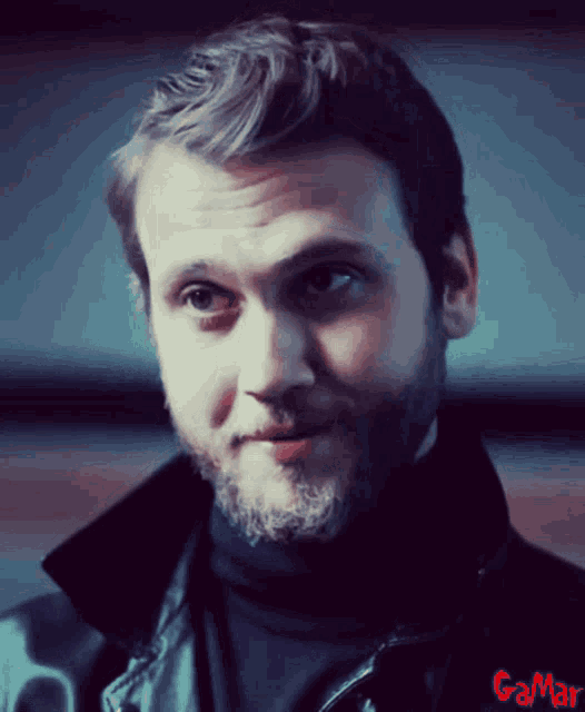a man with a beard is wearing a black turtleneck and a black leather jacket with gamar written on it