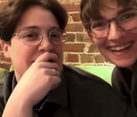 two people wearing glasses are smiling and covering their mouths with their hands