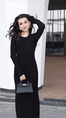 a woman in a long black dress is holding a small black bag