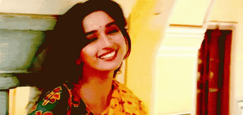 a woman in a yellow and green floral top smiles for the camera