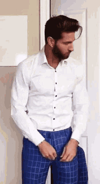 a man in a white shirt and blue plaid pants is standing in a doorway .