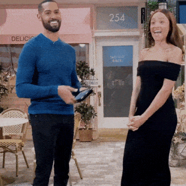 a man in a blue sweater stands next to a woman in a black dress in front of a door with the number 254 on it