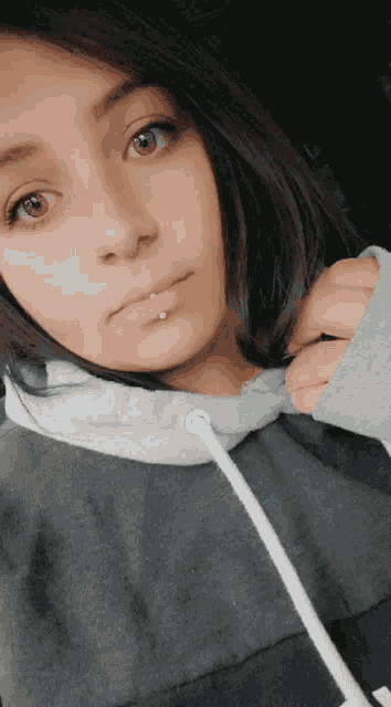 a girl with a piercing in her lip is wearing a gray hoodie