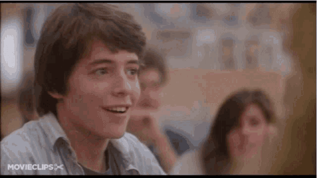 a young man is smiling in a classroom while sitting at a table .