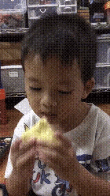 a young boy wearing a t-shirt that says ok is eating a piece of food