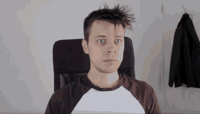 a young man sitting in a chair with his eyes wide open and his hair blowing in the wind