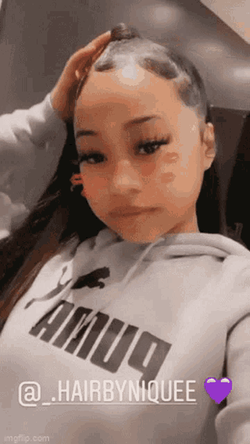 a girl wearing a grey puma hoodie is taking a selfie with her hand on her head .