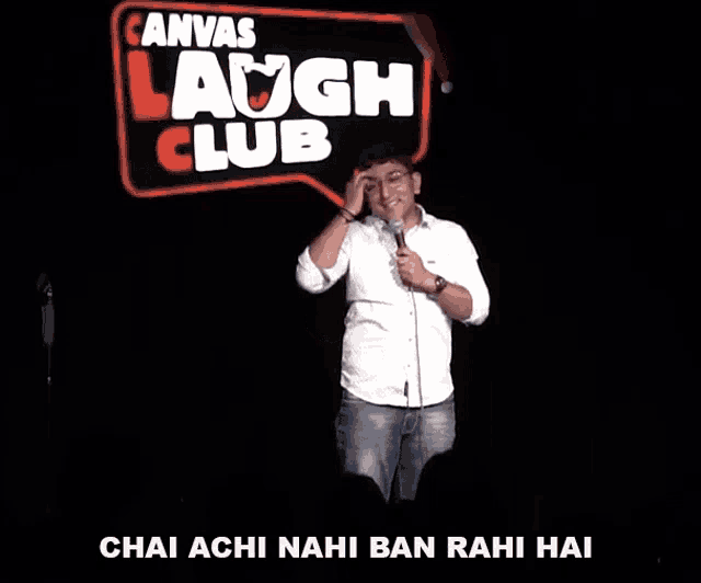 a man is holding a microphone in front of a canvas laugh club sign